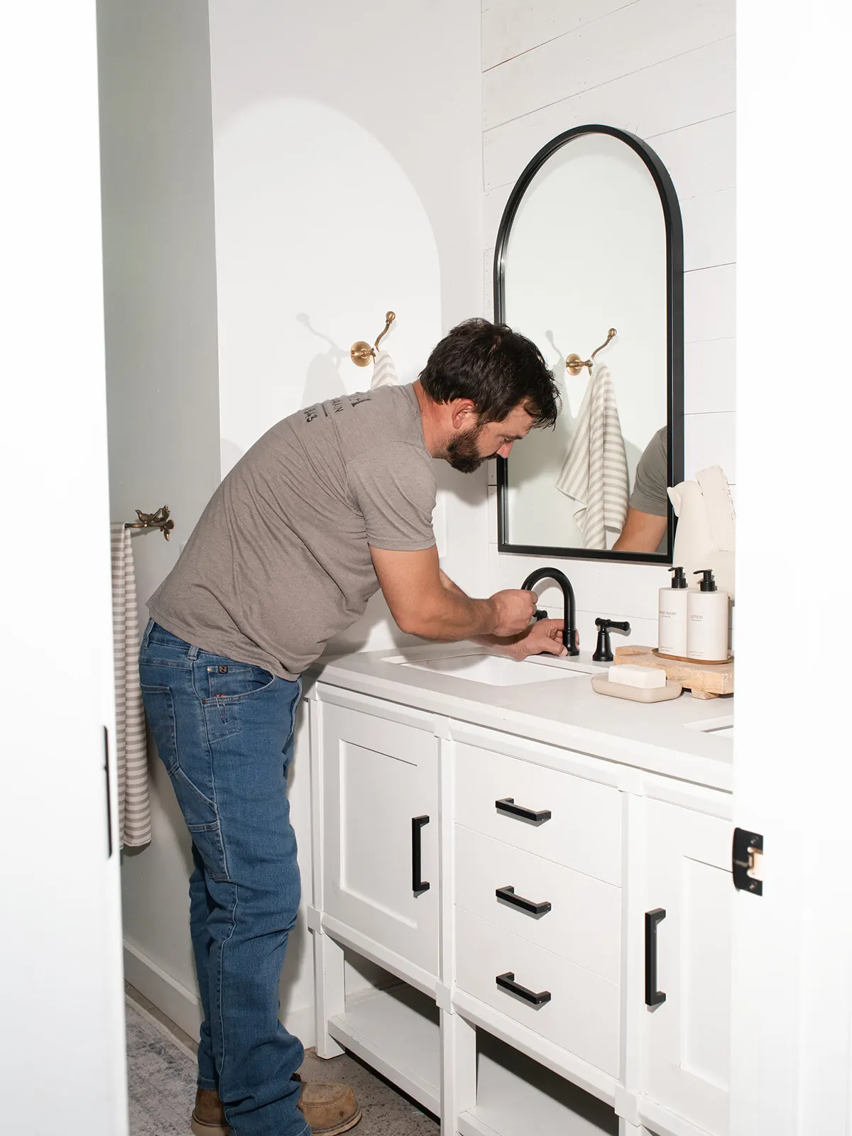 Luke Williams installing a matte black faucet on a white bathroom vanity