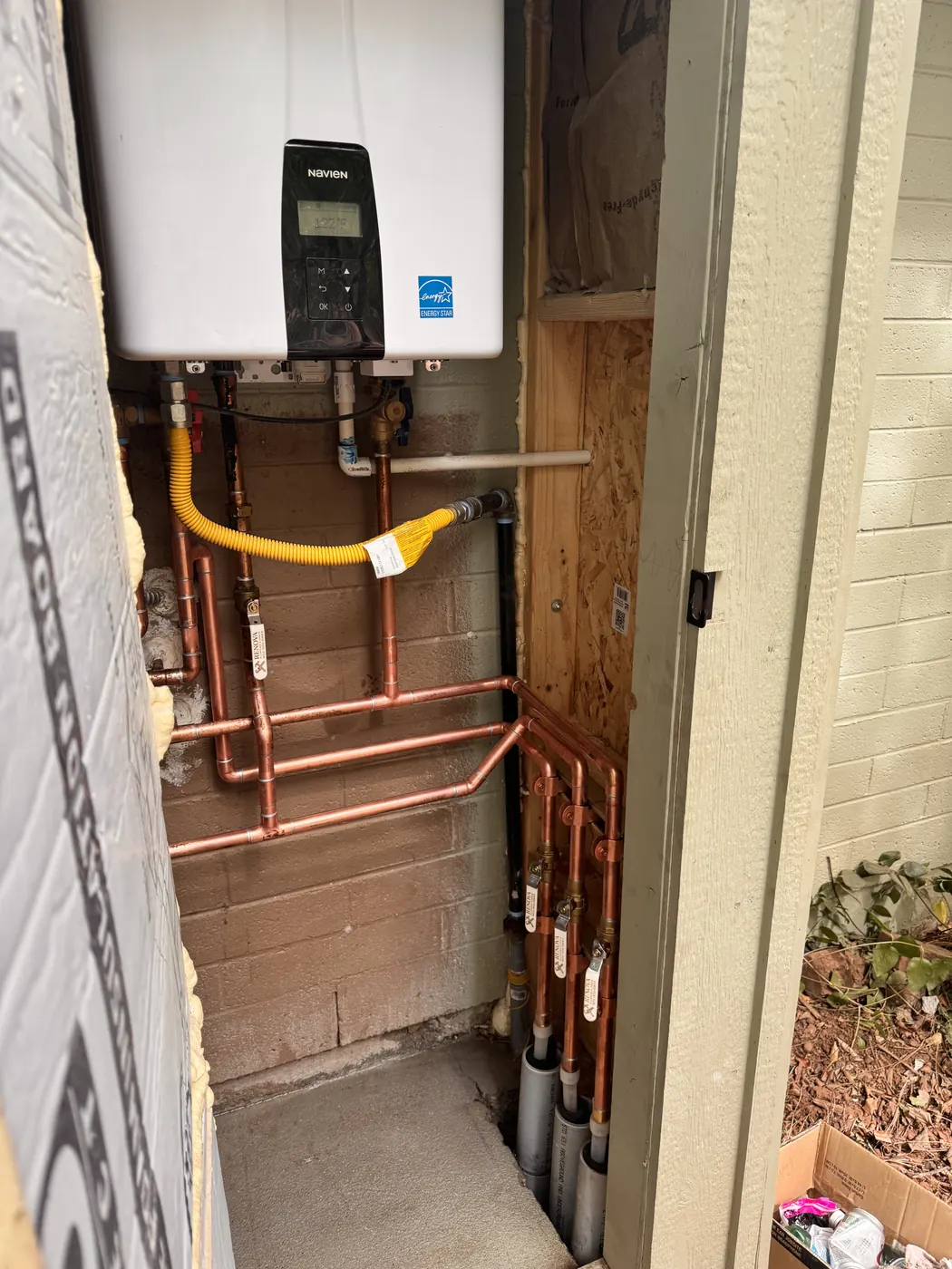 Tankless water heater in an exterior closet with a yellow gas connector and copper lines