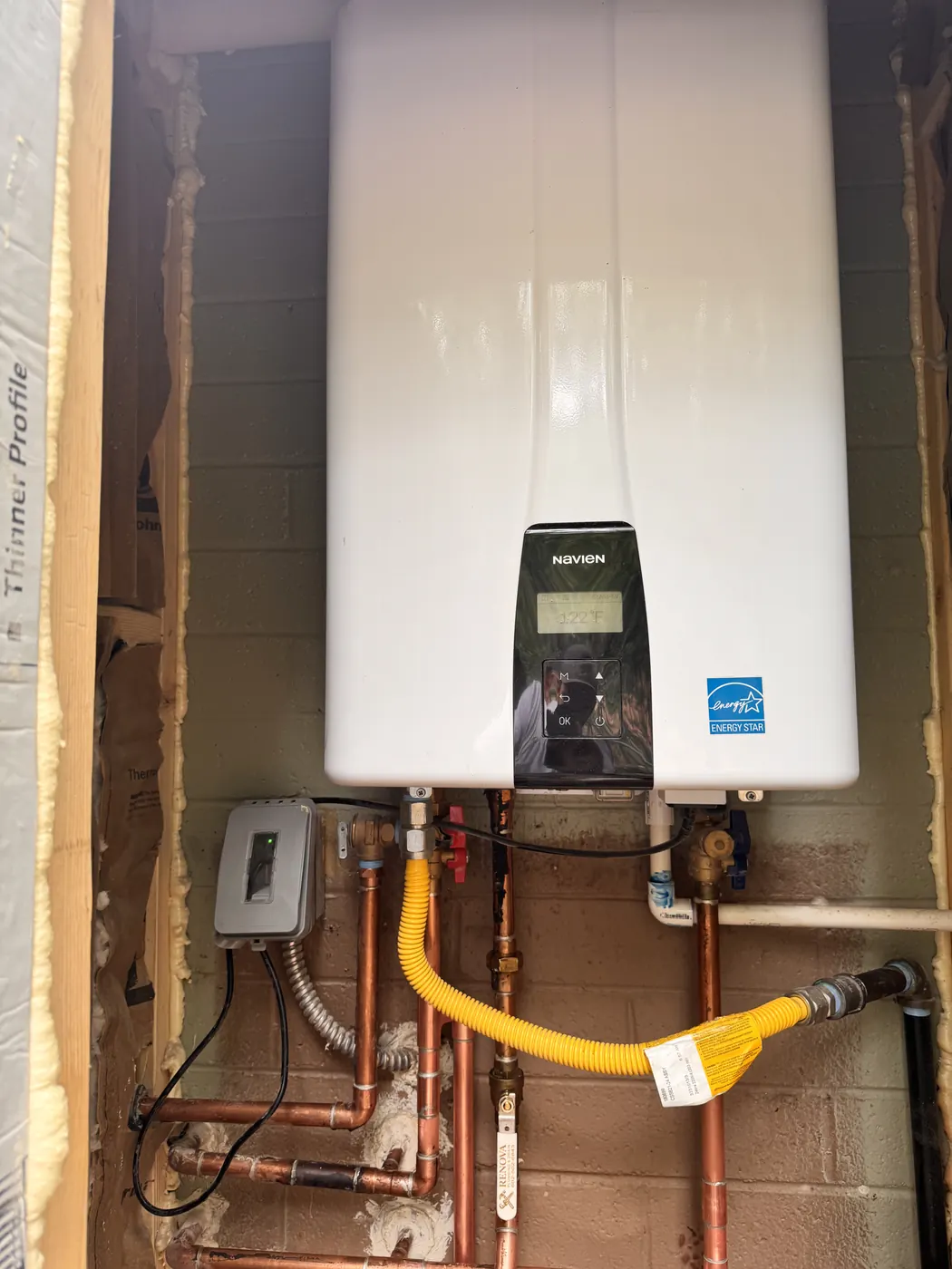 Tankless water heater in an exterior closet with copper piping and a yellow gas connector