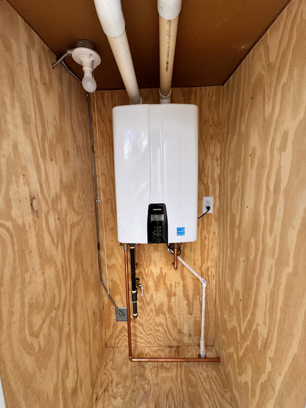 Tankless water heater mounted in a plywood enclosure with copper supply lines