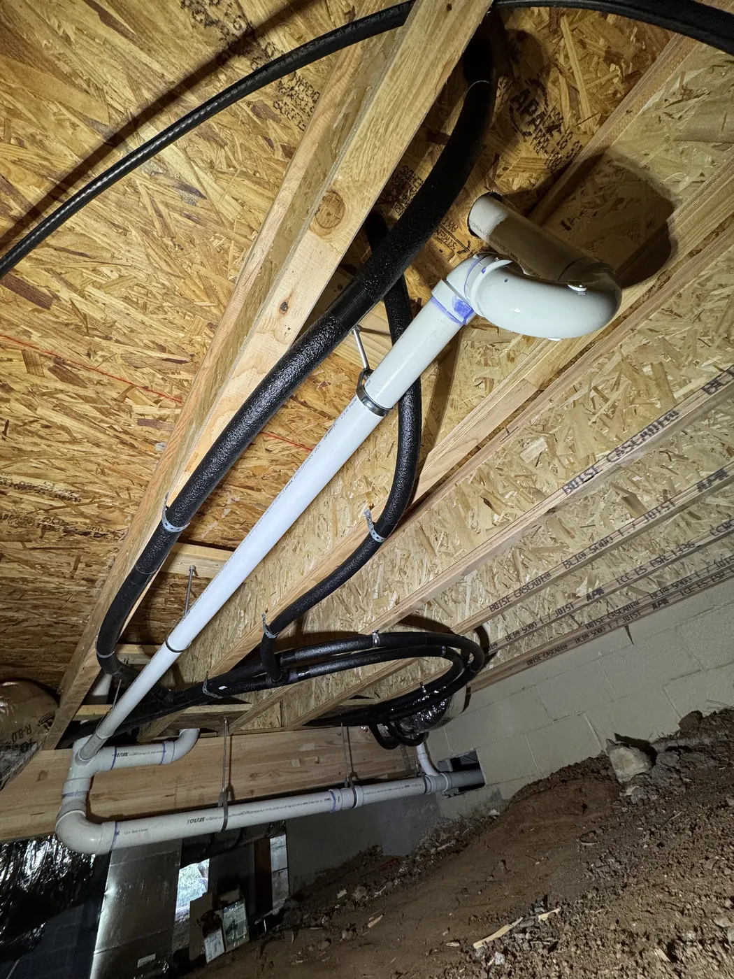New white PVC drain line and PEX water lines run under a raised floor
