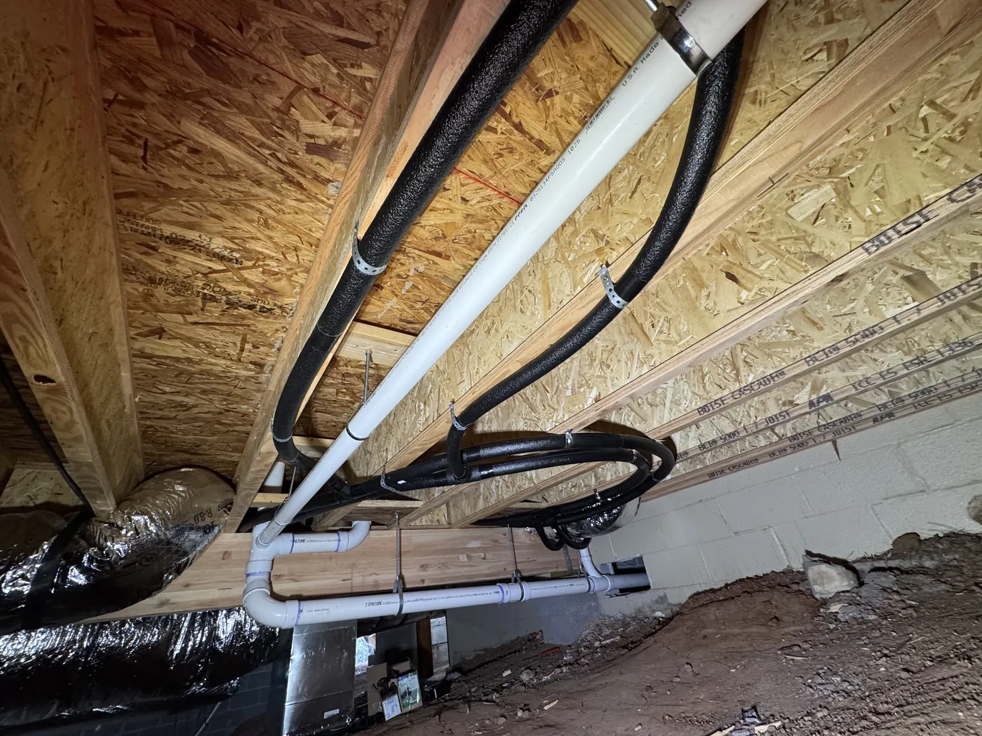 New PEX water supply runs and PVC drain line under a floor in a crawlspace